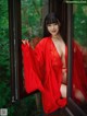 A woman in a red robe is posing by a window.