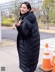 A woman in a long black coat standing in front of traffic cones.