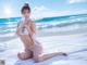 A woman in a white bikini sitting on a beach.